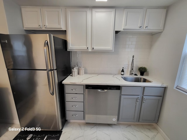 kitchen featuring light stone counters, stainless steel appliances, gray cabinets, and sink