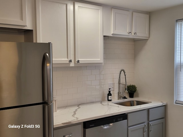 kitchen featuring sink, light stone counters, decorative backsplash, white cabinets, and appliances with stainless steel finishes