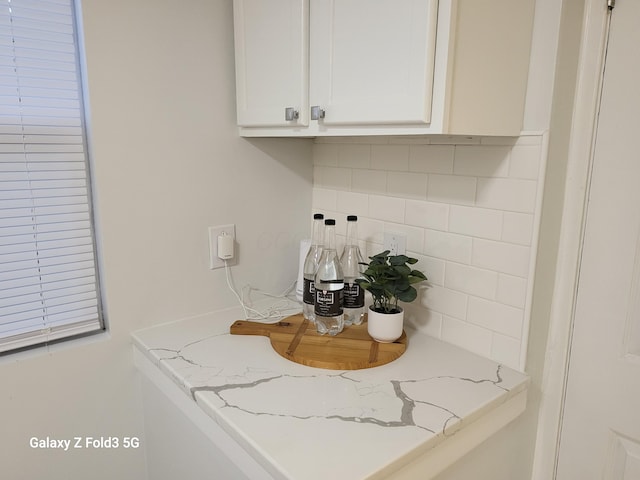 interior space with backsplash, light stone counters, and white cabinets