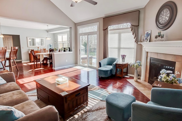 living room featuring ceiling fan, wood-type flooring, a tiled fireplace, and high vaulted ceiling