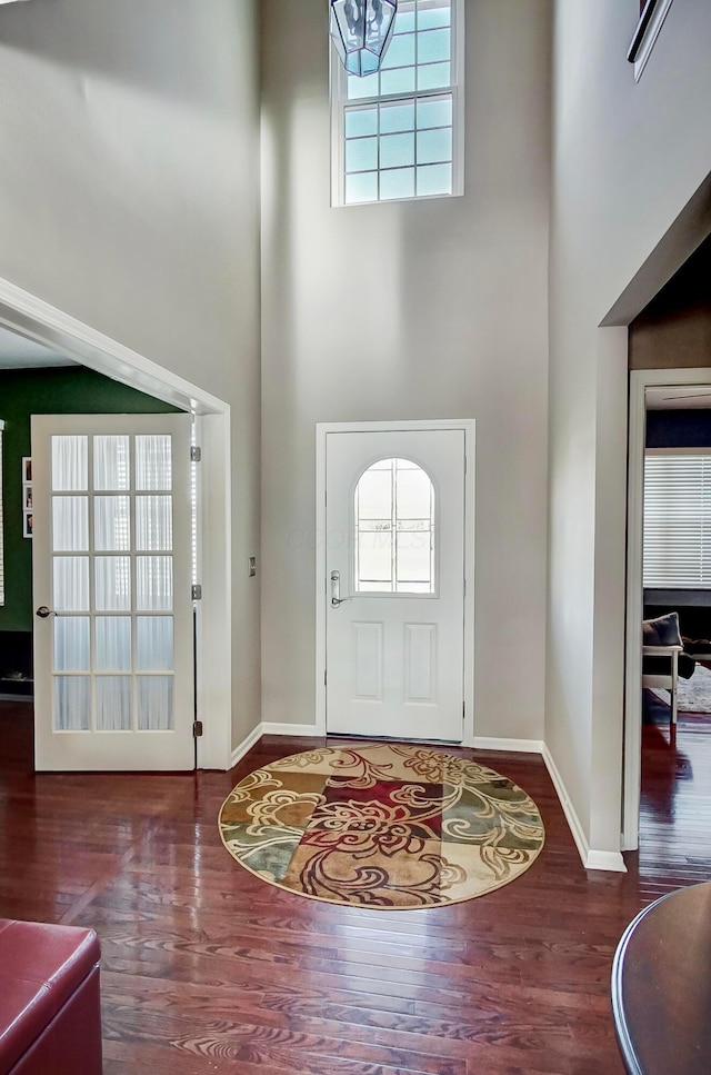 entrance foyer with a wealth of natural light, a towering ceiling, and dark wood-type flooring