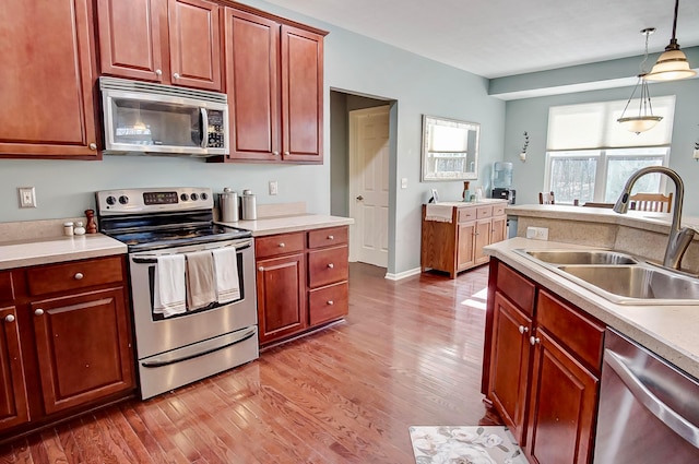 kitchen with hardwood / wood-style flooring, appliances with stainless steel finishes, sink, and hanging light fixtures