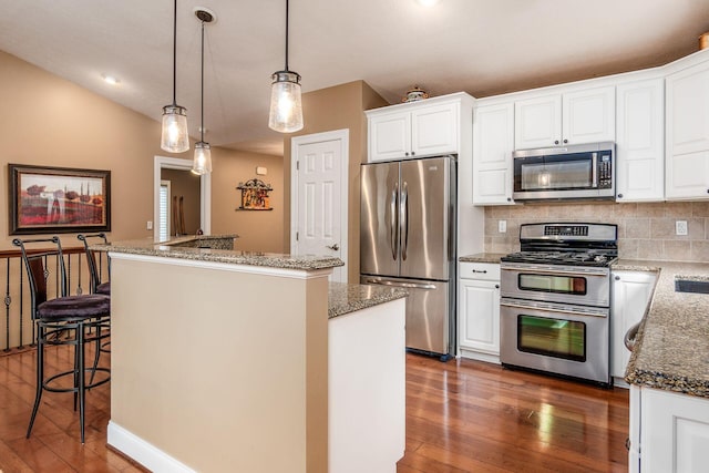 kitchen with dark wood-type flooring, hanging light fixtures, a kitchen island, white cabinetry, and stainless steel appliances