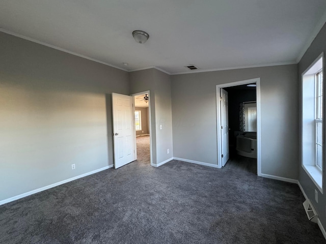 unfurnished bedroom featuring ensuite bathroom, dark carpet, crown molding, and multiple windows