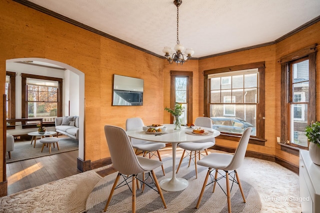 dining space with a wealth of natural light, ornamental molding, wood-type flooring, and an inviting chandelier