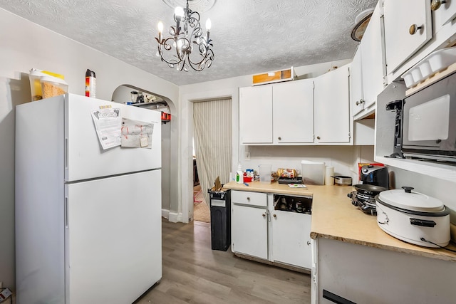 kitchen with hanging light fixtures, light wood-type flooring, white cabinets, and white fridge