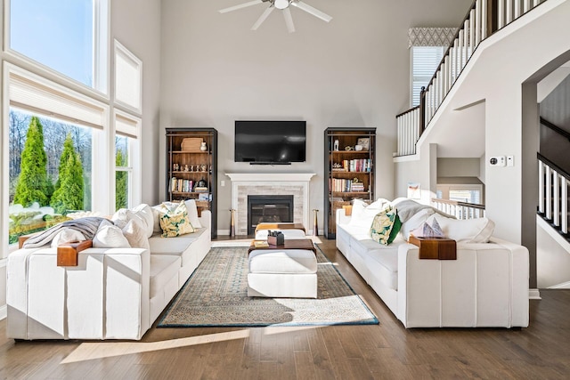 living room featuring hardwood / wood-style flooring, ceiling fan, a tile fireplace, and a high ceiling