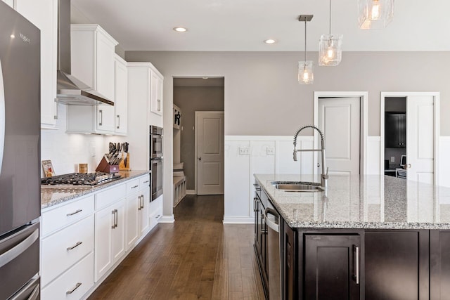 kitchen with dark hardwood / wood-style floors, wall chimney range hood, a kitchen island with sink, and stainless steel appliances