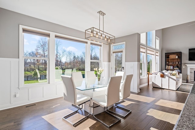 dining space featuring dark wood-type flooring, a notable chandelier, a healthy amount of sunlight, and a tiled fireplace