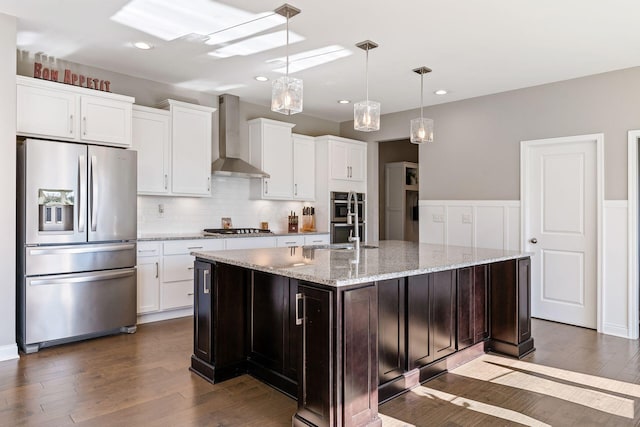 kitchen with dark hardwood / wood-style flooring, stainless steel appliances, a center island with sink, and wall chimney exhaust hood