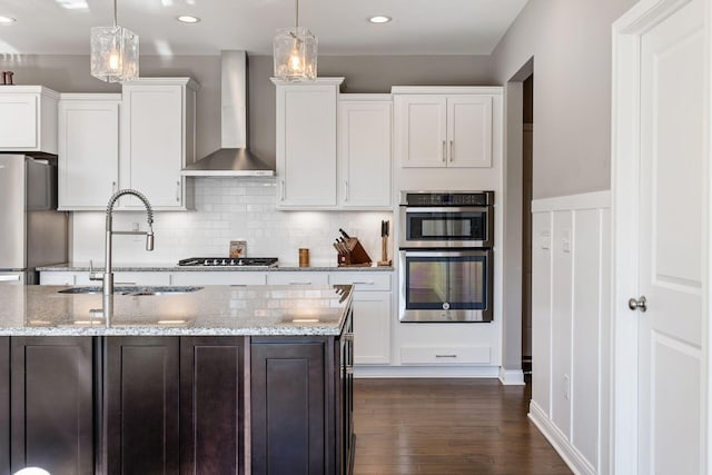 kitchen featuring sink, white cabinets, hanging light fixtures, and wall chimney range hood