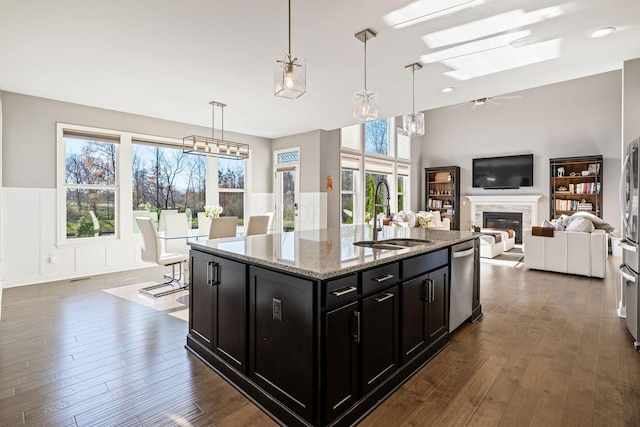 kitchen featuring a wealth of natural light, light stone counters, sink, and a center island with sink