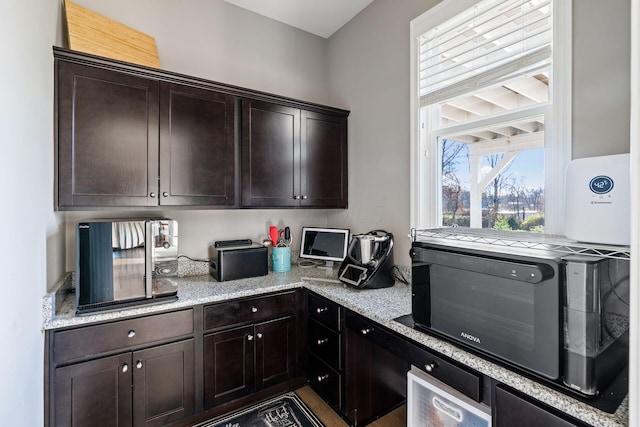 kitchen featuring light stone counters and dark brown cabinetry