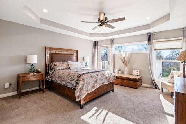 carpeted bedroom featuring ceiling fan, a tray ceiling, and multiple windows