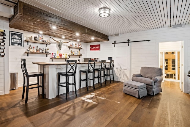 bar featuring a barn door, dark hardwood / wood-style flooring, wooden ceiling, and wooden walls