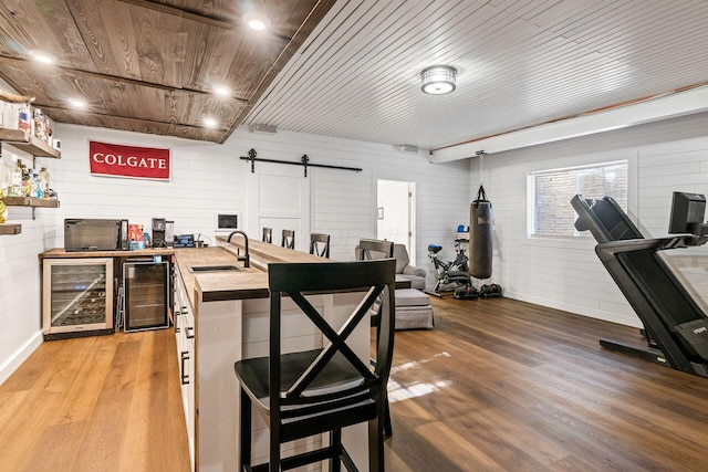 bar with sink, a barn door, light hardwood / wood-style floors, butcher block counters, and beverage cooler