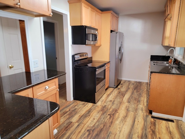 kitchen with appliances with stainless steel finishes, light brown cabinetry, dark stone counters, sink, and light hardwood / wood-style flooring