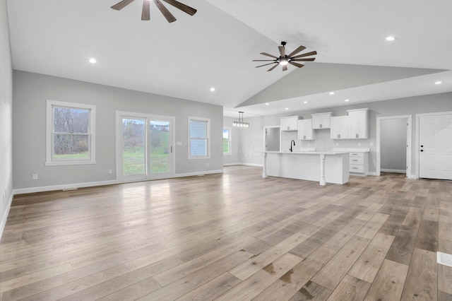 unfurnished living room featuring sink, light wood-type flooring, ceiling fan with notable chandelier, and high vaulted ceiling