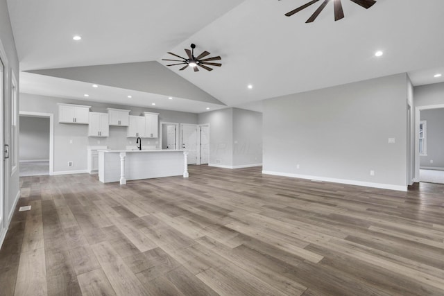 unfurnished living room with sink, hardwood / wood-style flooring, high vaulted ceiling, and ceiling fan