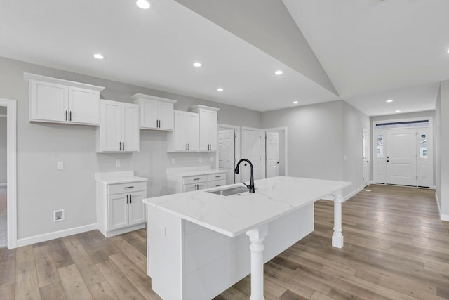 kitchen featuring white cabinetry, sink, a kitchen island with sink, light stone counters, and a breakfast bar area