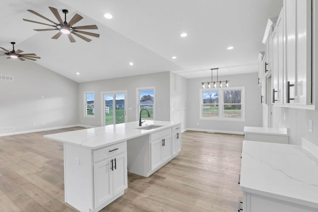 kitchen with sink, white cabinetry, vaulted ceiling, and an island with sink