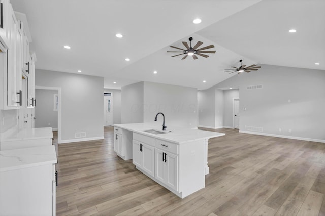 kitchen with light stone countertops, a spacious island, white cabinetry, light hardwood / wood-style floors, and sink