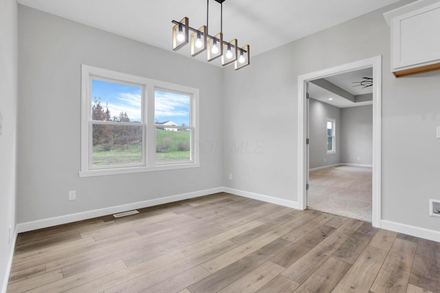 unfurnished dining area with light hardwood / wood-style flooring and a raised ceiling