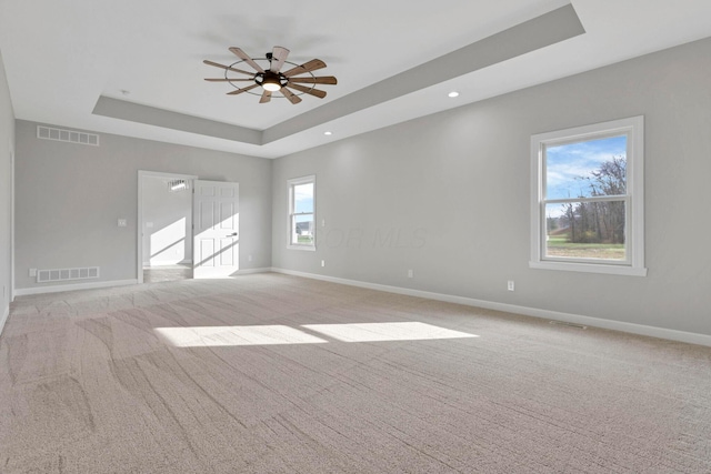 spare room with light carpet, ceiling fan, and a raised ceiling