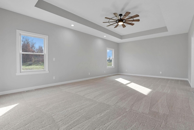 unfurnished room featuring ceiling fan, light colored carpet, and a tray ceiling