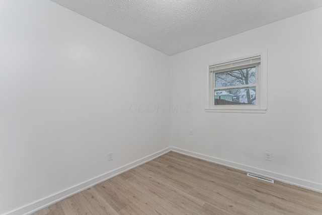 empty room with a textured ceiling and light hardwood / wood-style flooring