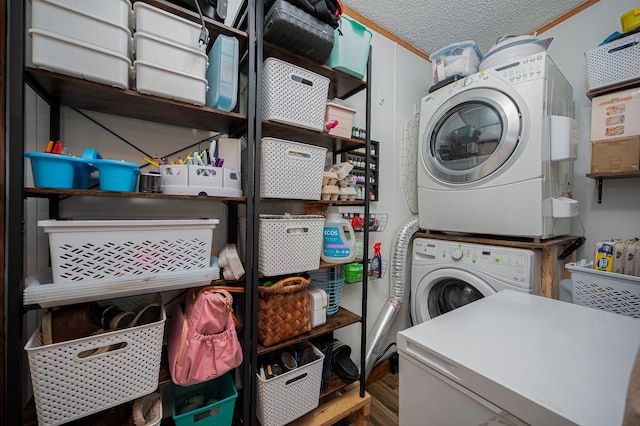 laundry room featuring stacked washer / drying machine, ornamental molding, and a textured ceiling