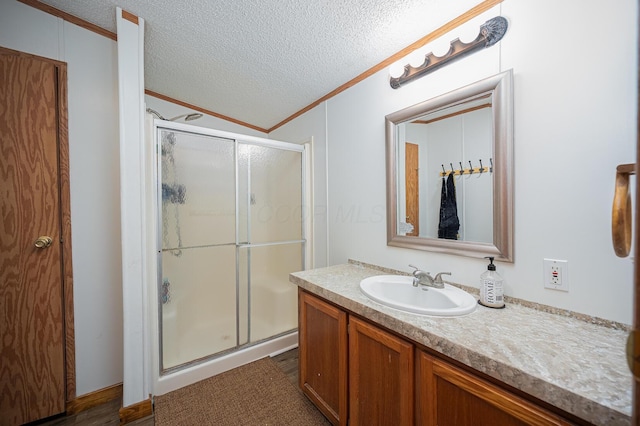 bathroom featuring vanity, a shower with door, ornamental molding, and a textured ceiling