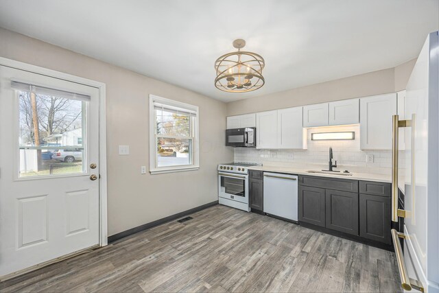 kitchen featuring white appliances, sink, hardwood / wood-style floors, white cabinetry, and hanging light fixtures