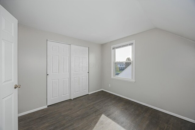 unfurnished bedroom with dark hardwood / wood-style flooring, lofted ceiling, and a closet