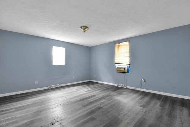 empty room with a textured ceiling, cooling unit, and dark wood-type flooring