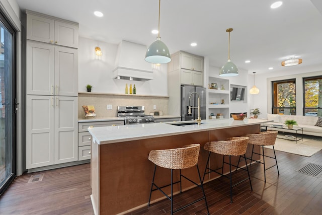 kitchen with a breakfast bar, a kitchen island with sink, dark wood-type flooring, hanging light fixtures, and stainless steel appliances