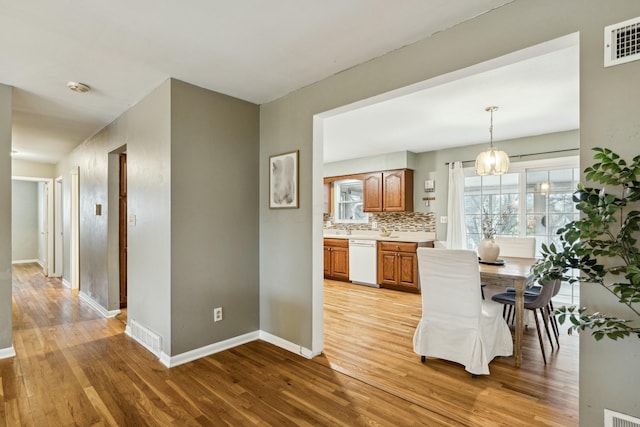 kitchen with dishwasher, backsplash, hanging light fixtures, and light hardwood / wood-style flooring