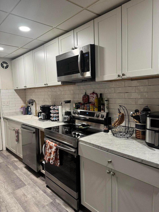 kitchen featuring light wood-type flooring, a paneled ceiling, light stone counters, stainless steel appliances, and white cabinetry