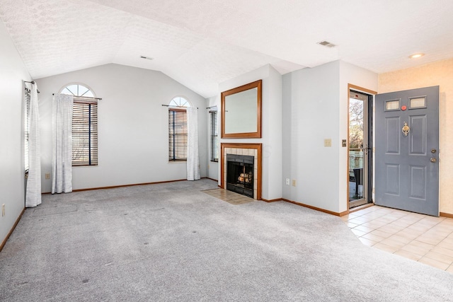 unfurnished living room with lofted ceiling, a tile fireplace, a textured ceiling, and light carpet