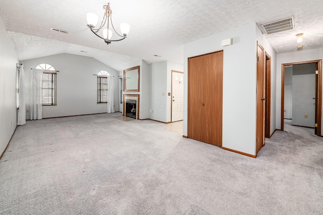 unfurnished living room with a tile fireplace, a notable chandelier, lofted ceiling, a textured ceiling, and light carpet