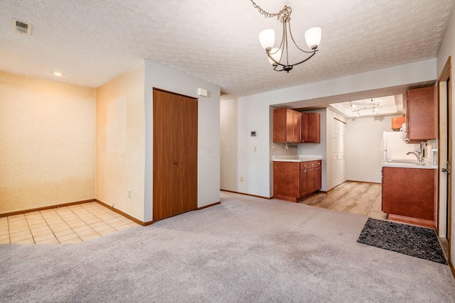 kitchen featuring sink, a notable chandelier, a textured ceiling, decorative light fixtures, and light carpet