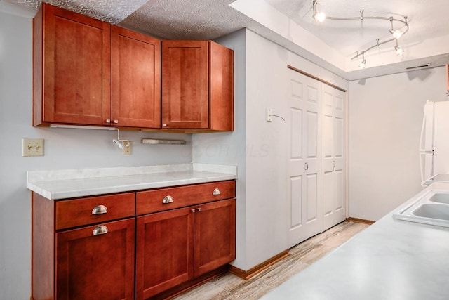 kitchen featuring sink, white fridge, light hardwood / wood-style floors, and a textured ceiling