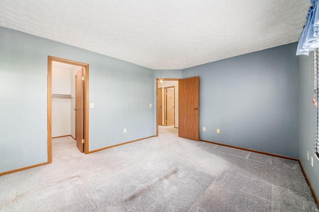 unfurnished bedroom featuring a spacious closet, a textured ceiling, light carpet, and a closet