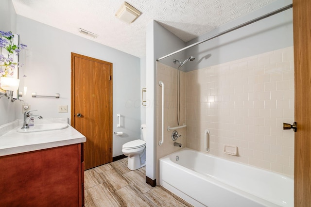 full bathroom with vanity, tiled shower / bath combo, a textured ceiling, and toilet