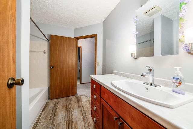 bathroom with vanity, a textured ceiling, and tiled shower / bath