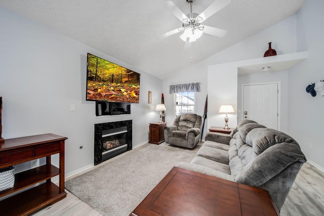 living room with ceiling fan, a textured ceiling, a fireplace, and light hardwood / wood-style flooring