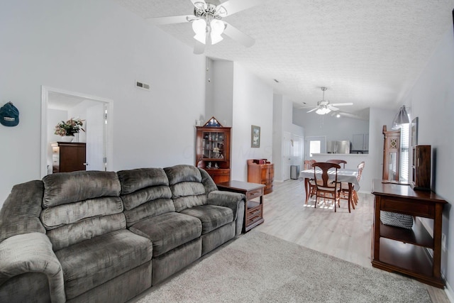 living room featuring ceiling fan, high vaulted ceiling, light hardwood / wood-style floors, and a textured ceiling