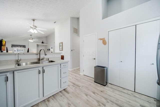 kitchen featuring lofted ceiling, sink, white cabinetry, a textured ceiling, and light wood-type flooring