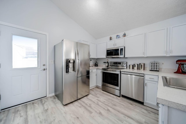 kitchen with appliances with stainless steel finishes, white cabinetry, lofted ceiling, light hardwood / wood-style floors, and a textured ceiling