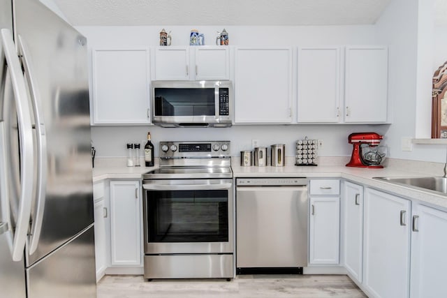 kitchen with sink, white cabinetry, a textured ceiling, light wood-type flooring, and stainless steel appliances